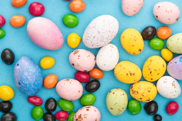 Draufsicht auf helle Bonbons, bunte Hühner- und Wachteleier auf blauem Hintergrund — Stockfoto