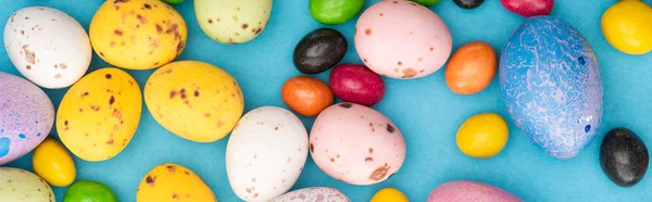 Top view of bright candies, colorful chicken and quail eggs on blue background, panoramic shot — Stock Photo