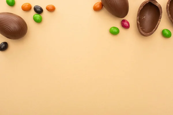 Top view of chocolate eggs and colorful candies on beige background — Stock Photo