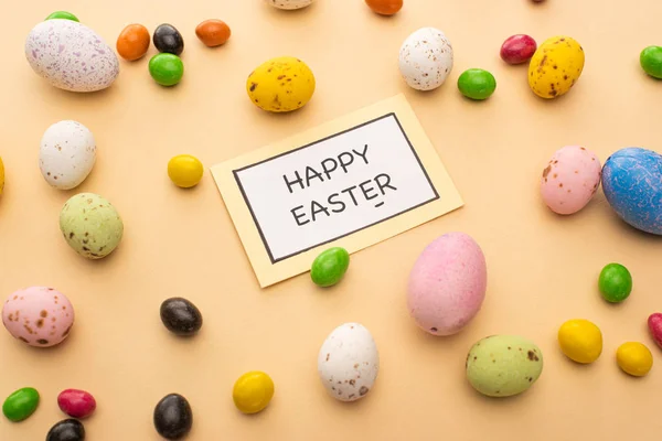 Card with happy easter lettering and bright candies on beige background — Stock Photo