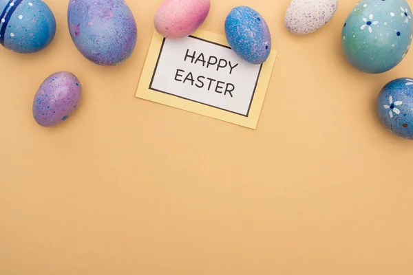 Vue du dessus de la carte avec joyeux lettrage de Pâques et oeufs de Pâques sur fond beige — Photo de stock