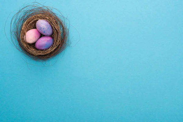 Top view of nest with colorful Easter eggs on blue background — Stock Photo