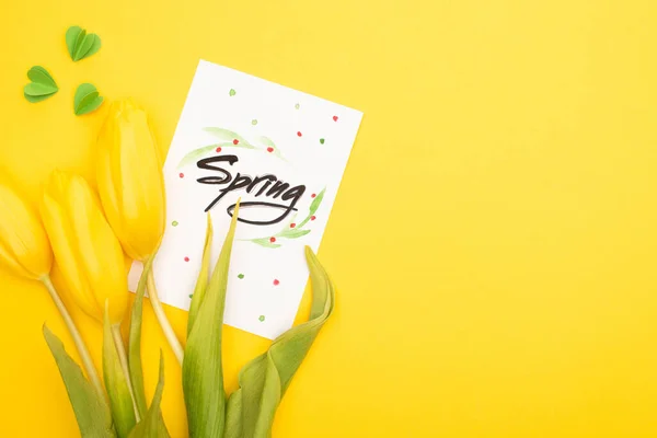 Top view of card with spring lettering, tulips and decorative green hearts on yellow background — Stock Photo