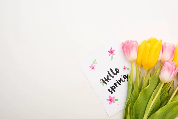 Top view of card with hello spring lettering near yellow and pink tulips on white background — Stock Photo