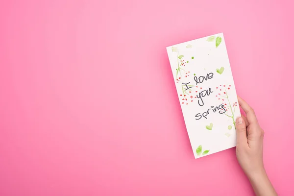 Vista parcial de la mujer que sostiene la tarjeta con I love you spring lettering on pink - foto de stock