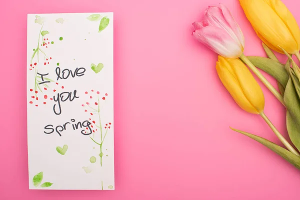 Vista dall'alto di tulipani e carta con ti amo lettering primaverile su rosa — Foto stock