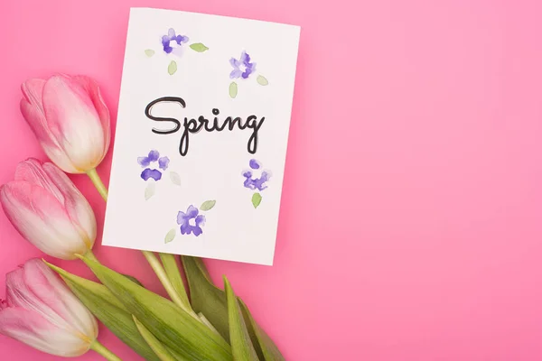 Draufsicht auf Blumen und Karte mit Frühlingsschrift auf rosa Hintergrund — Stockfoto