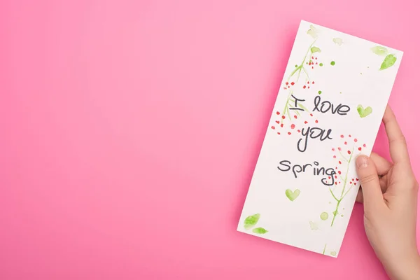 Vue partielle de la carte avec je t'aime lettrage de printemps dans la main de la femme sur fond rose — Photo de stock