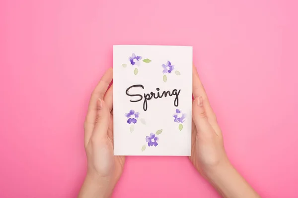 Частковий вигляд листівки з весняним написанням у жіночих руках на рожевому фоні — стокове фото
