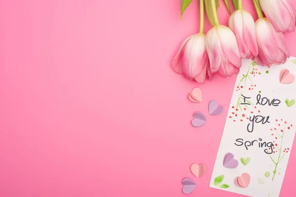 Vista superior de tulipanes, tarjeta con I love you letras de primavera y corazones decorativos de colores sobre fondo rosa - foto de stock
