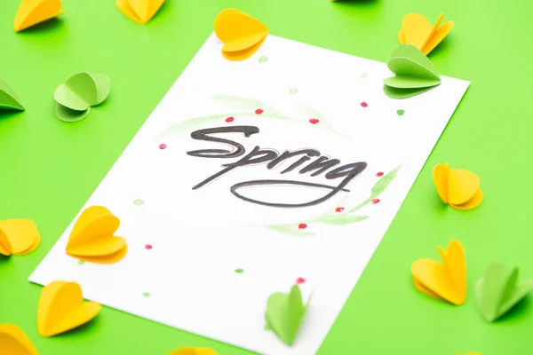 Selective focus of card with spring lettering and decorative hearts on green background — Stock Photo