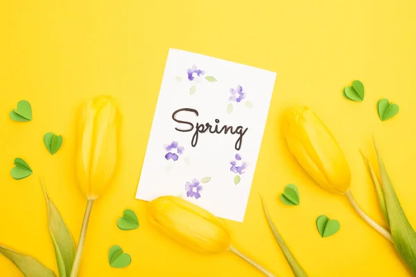 Draufsicht auf Tulpen, Karte mit Frühlingsschrift und dekorativen grünen Herzen auf gelbem Hintergrund — Stockfoto