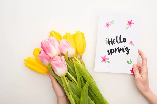 Vue recadrée de la femme tenant bouquet de tulipes et carte avec lettrage bonjour printemps sur fond blanc — Photo de stock