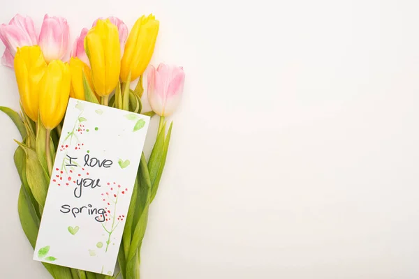 Vue du dessus de la carte avec je t'aime lettrage printemps sur bouquet de tulipes sur fond blanc — Photo de stock