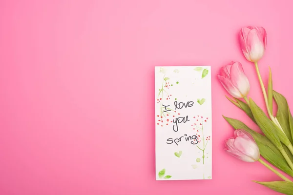 Top view of tulips and card with I love you spring lettering on pink background — Stock Photo