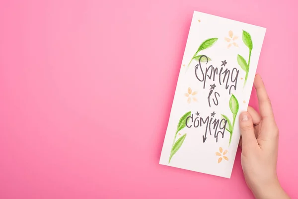 Cropped view of woman holding card with spring is coming lettering on pink background — Stock Photo