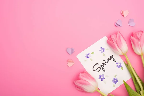 Draufsicht auf Tulpen, Karte mit Frühlingsschrift und dekorativen Herzen auf rosa — Stockfoto