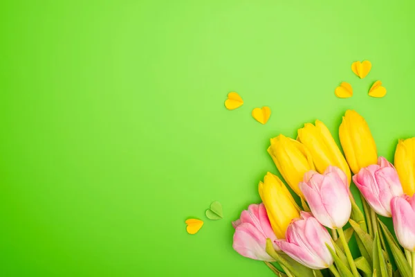 Vista superior de tulipanes amarillos y rosados con corazones decorativos sobre fondo verde, concepto de primavera - foto de stock