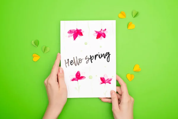 Ausgeschnittene Ansicht einer Frau mit Karte mit Hallo-Frühling-Schriftzug auf grünem Hintergrund — Stockfoto