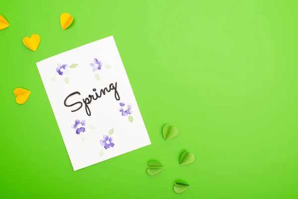 Top view of card with spring lettering and decorative hearts on green background — Stock Photo