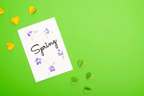 Top view of card with spring lettering and decorative hearts on green background — Stock Photo