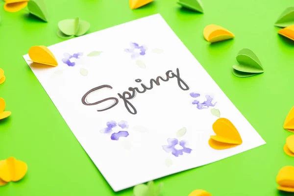 Selective focus of card with spring lettering and decorative hearts on green background — Stock Photo