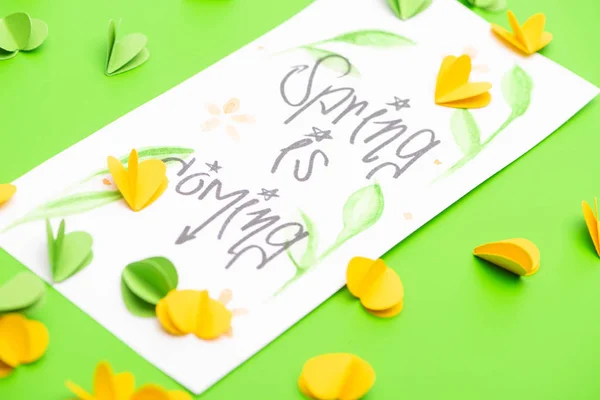 Selective focus of card with spring is coming lettering and decorative hearts on green background — Stock Photo