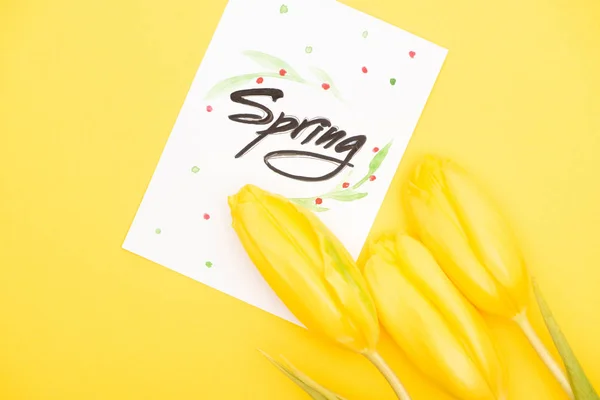 Vue du dessus de la carte avec lettrage de printemps et tulipes sur fond jaune — Photo de stock