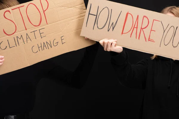 Vista recortada de las mujeres con pancartas con detener el cambio climático y cómo te atreves a escribir aislado en negro, concepto de calentamiento global - foto de stock