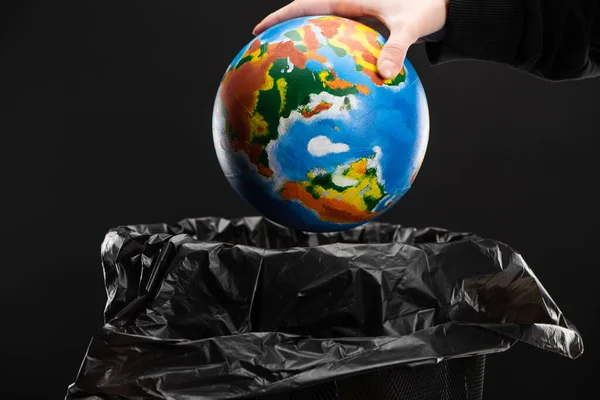 Cropped view of woman throwing away globe in trash bin isolated on black, global warming concept — Stock Photo