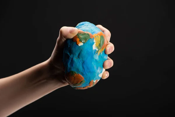 Partial view of woman compressing plasticine globe in hand isolated on black, global warming concept — Stock Photo