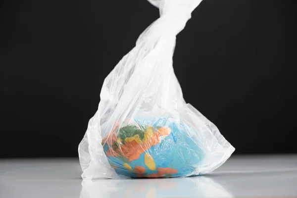 Пластиковий глобус у поліетиленовому пакеті ізольований на чорному, концепція глобального потепління — стокове фото