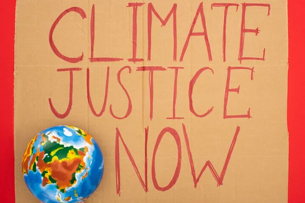 Top view of globe and placard with climate justice now lettering on red background, global warming concept — Stock Photo