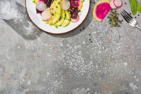 Vista superior de salada de rabanete fresco com verduras e abacate na superfície de concreto cinza com vidro de água e garfo — Fotografia de Stock