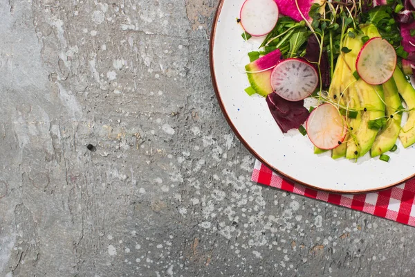 Top view of fresh radish salad with greens and avocado on grey concrete surface with fork and napkin — Stock Photo