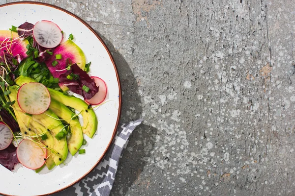 Draufsicht auf frischen Rettichsalat mit Gemüse und Avocado auf grauer Betonoberfläche mit Gabel und Serviette — Stockfoto
