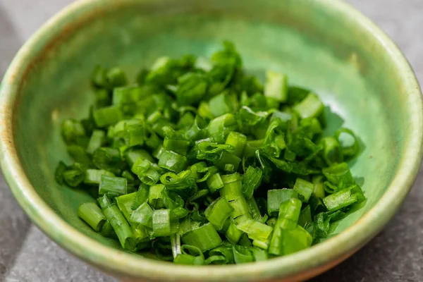Close up view of fresh cut green onion in bowl on grey concrete surface — Stock Photo