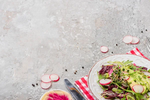 Fresh radish salad with greens and avocado served on napkin with cutlery on grey concrete surface — Stock Photo