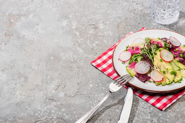 Salada de rabanete fresco com verduras e abacate servido em guardanapo com talheres perto de água na superfície de concreto cinza — Fotografia de Stock