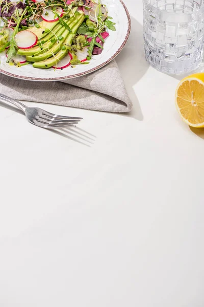 Salade de radis frais avec légumes verts et avocat sur une surface blanche avec citron et eau — Photo de stock