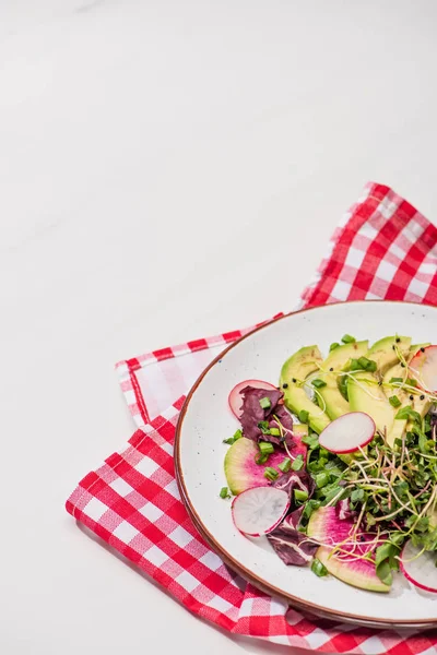 Frischer Rettichsalat mit Gemüse und Avocado auf Teller auf weißer Oberfläche mit Serviette — Stockfoto