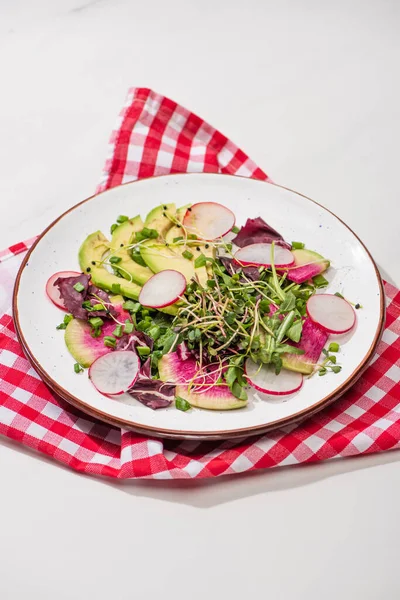 Свіжий салат з редькою з зеленню та авокадо на тарілці на білій поверхні з серветкою — стокове фото