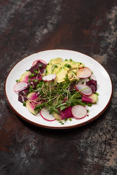 Fresh radish salad with greens and avocado on plate on weathered surface — Stock Photo