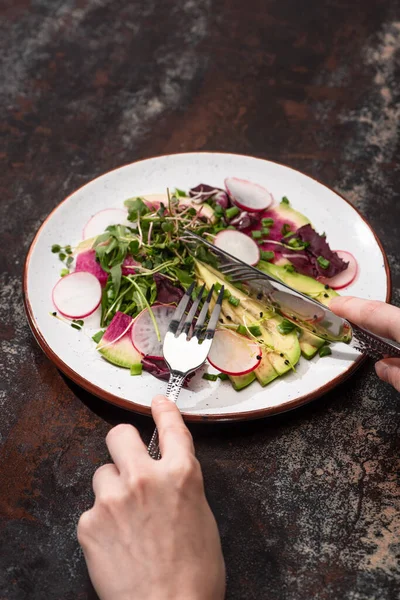 Cropped view of woman eating fresh radish salad with greens and avocado with cutlery — Stock Photo