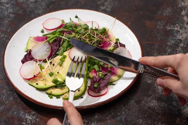 Abgeschnittene Ansicht einer Frau, die frischen Rettichsalat mit Gemüse und Avocado mit Besteck isst — Stockfoto