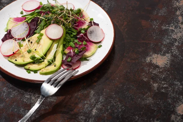 Fresh radish salad with greens and avocado on plate on weathered surface with fork — Stock Photo