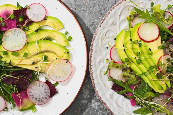 Vista dall'alto d'insalata di ravanello fresca con verdi e avocado su piatti su superficie concreta grigia — Foto stock