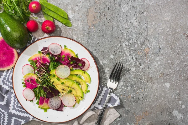 Vue de dessus de la salade de radis frais avec légumes verts et avocats près de la fourchette et légumes sur la surface en béton gris — Photo de stock