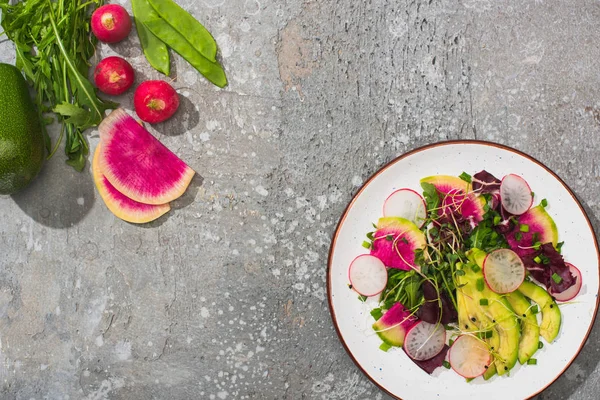 Vista superior de ensalada de rábano fresco con verdura y aguacate cerca de verduras en superficie de hormigón gris - foto de stock