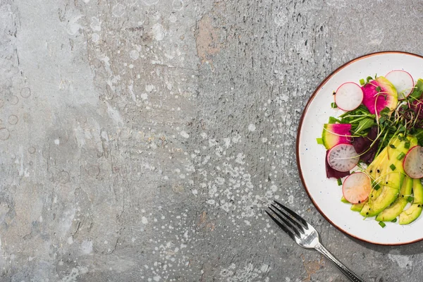 Vue de dessus de salade de radis frais avec légumes verts et avocat près de la fourche sur la surface de béton gris — Photo de stock